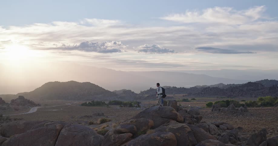 A lone hiker stands on a rocky outcrop admiring the vast desert landscape at sunset