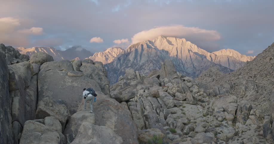 Male hiker climbs boulders in a boulder strewn valley under a cloudy autumn sky