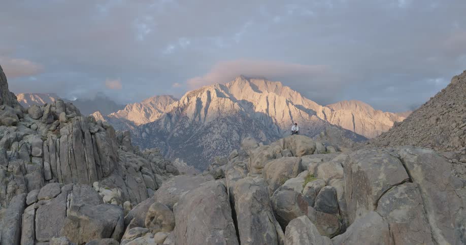 Man sits on one of the boulders forming piles in a valley in a mountain range on a cloudy autumn day