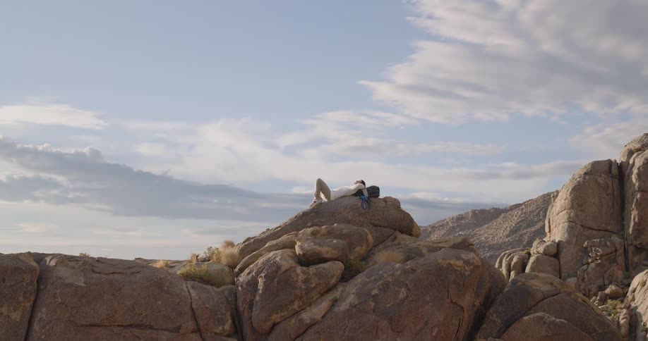 Person lying on rock in arid terrain under partly cloudy sky