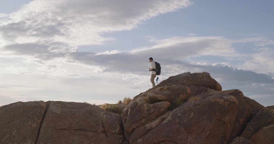 Man with a backpack explores rocky formations under a cloudy sky