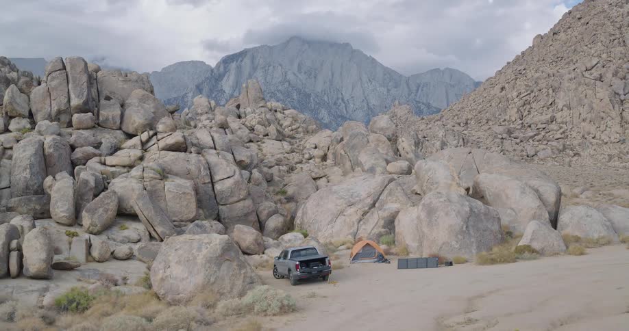 Campsite with pickup truck tent and gear in rocky area surrounded by mountains