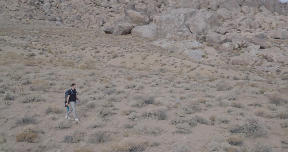 Male photographer camping near a rock formation walks across a field before stopping to take a picture