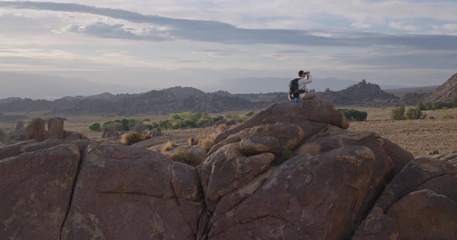 The man uses binoculars on top of the stack of boulders