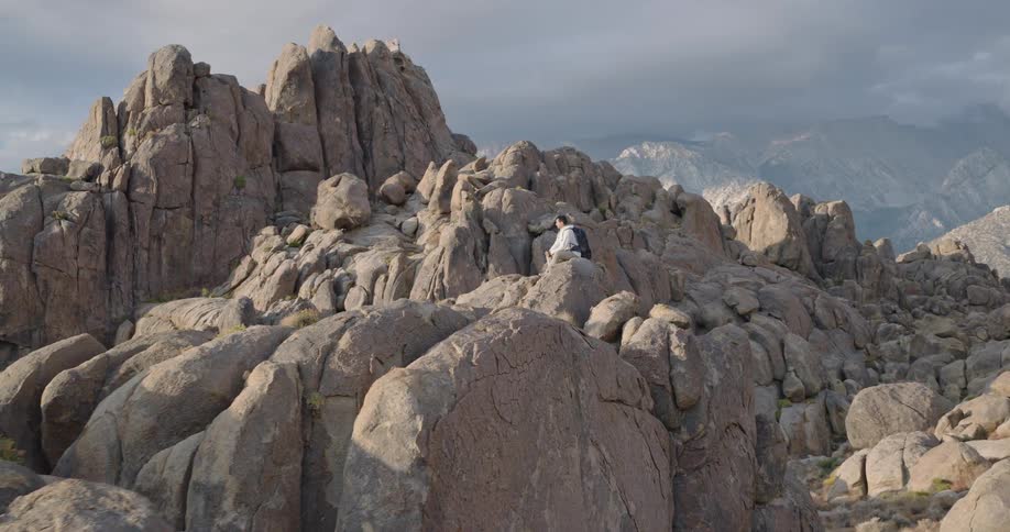 The video is an extreme long shot of a mountainous landscape with a prominent foreground of rounded jagged boulders in the background much taller snowdusted mountains rise up toward a moody cloudy sky