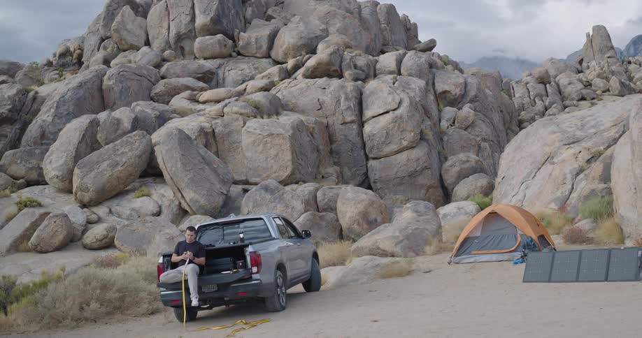 A man sets up camp in a rocky mountainous landscape with his truck a tent and solar panels