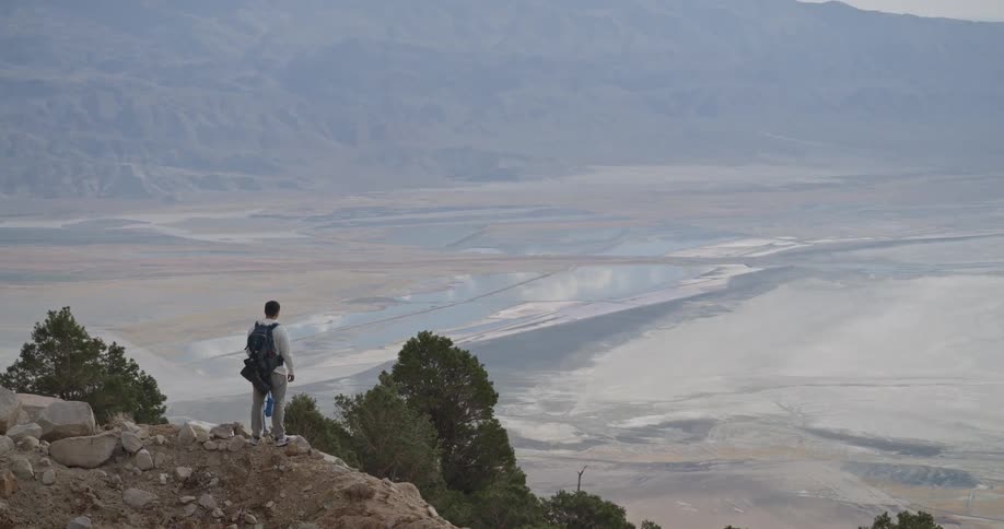 Person with backpack overlooking arid valley with rock formations and sparse vegetation