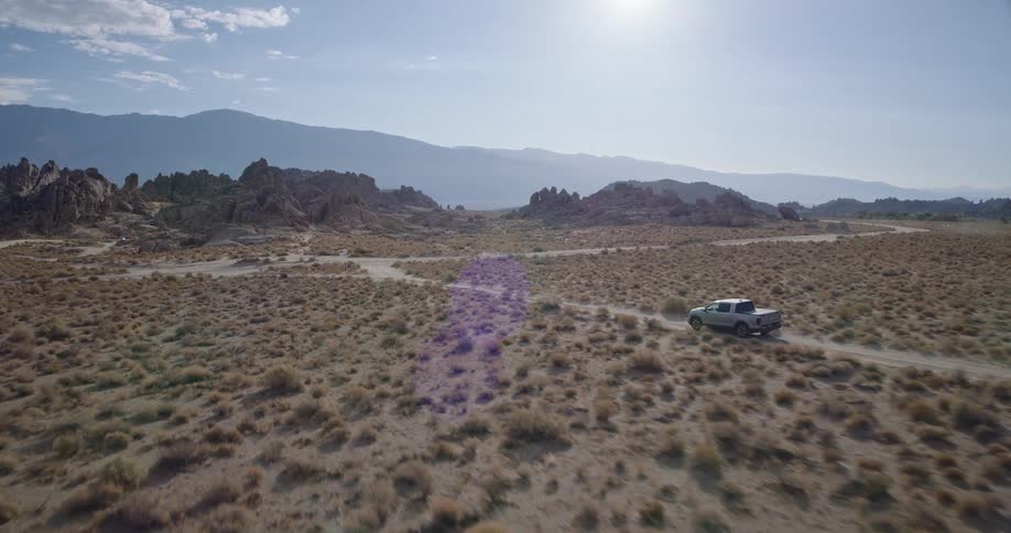 A truck drives through a dirt road in the wilderness at midday