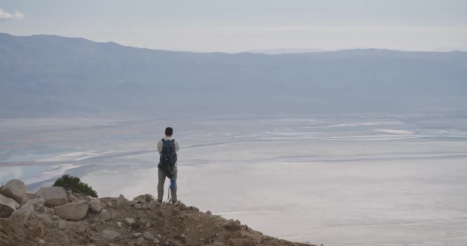 Person with backpack on rocky overlook observing vast plain with mountains in the distance