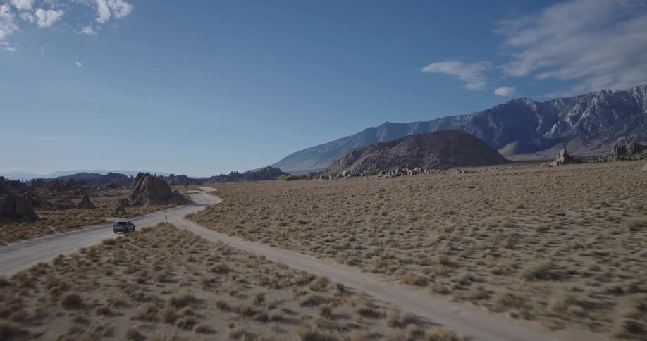 Vehicle on dirt road crossing arid landscape with mountains in the background