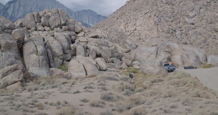 A hiker with a prosthetic leg and a backpack walks away from a campsite in a vast rocky mountainous landscape
