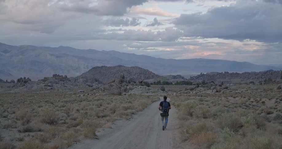 The man is walking on the trail towards the mountains