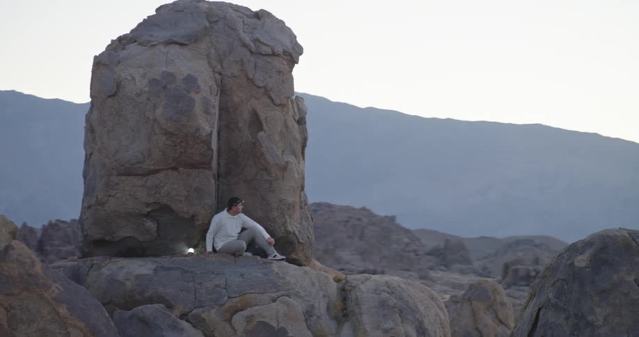 Man wearing a headlamp sits on a rock formation located near a dirt road on a foggy day