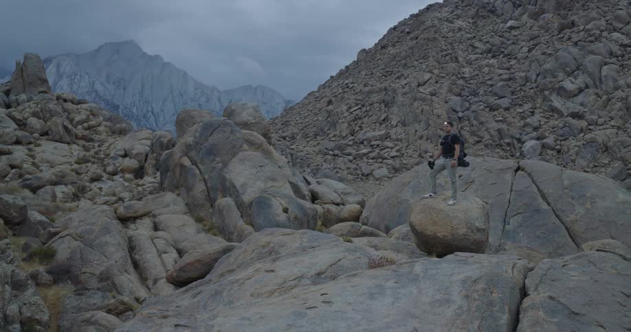 Man on rock in mountainous terrain surrounded by boulders and steep slopes