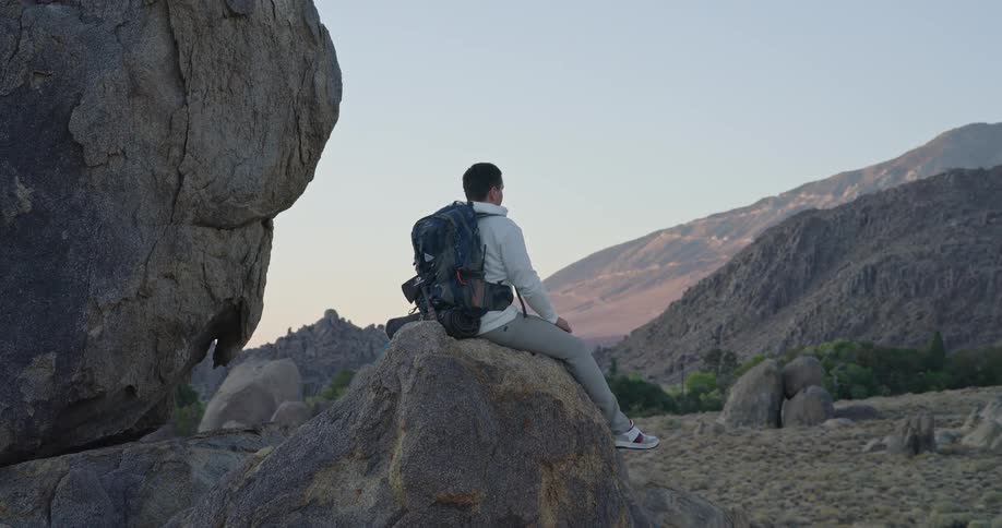 Man sitting on a rock looking at a mountain range outdoors during dusk or dawn