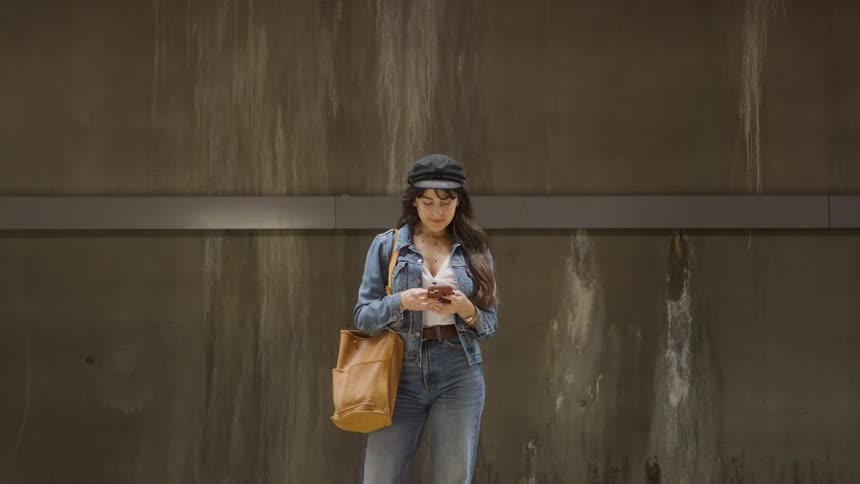 Woman wearing denim clothes and a hat standing up and using a smartphone