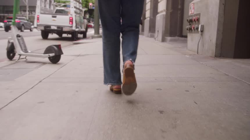 Close up of a womans legs as she walks on a sidewalk in a city during daytime