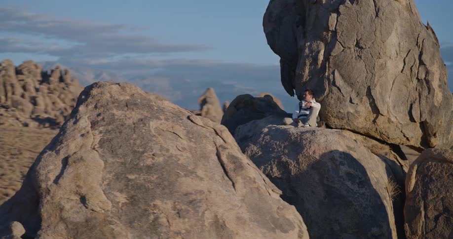 Man sits on a rock formation of stacked boulders on a cloudy autumn day