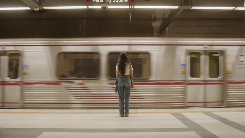 Woman standing on subway platform in front of moving train at pershing square station