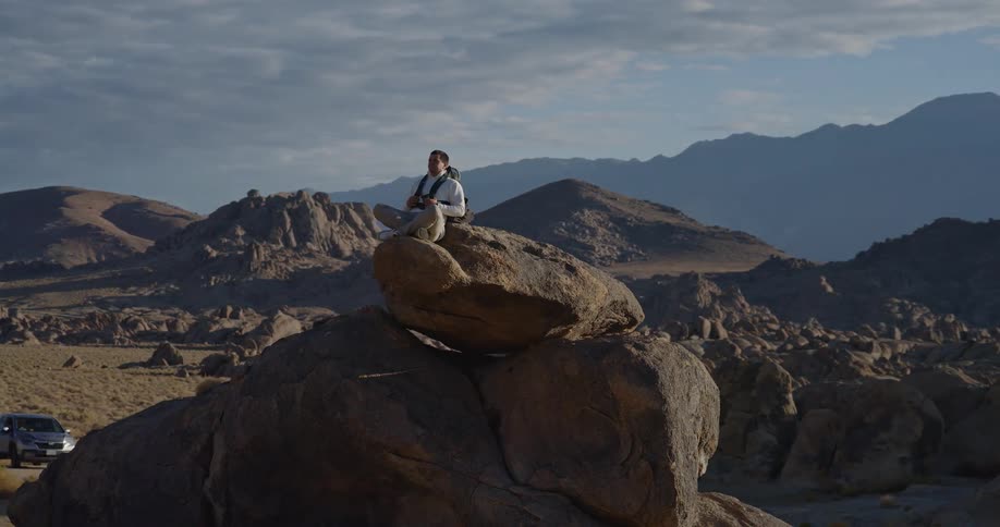 Male backpacker sits on a rock formation in a boulder field on a hazy day
