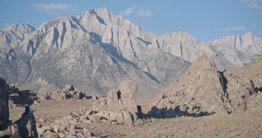 Man among rocks in arid mountainous landscape with peaks in the background under clear sky