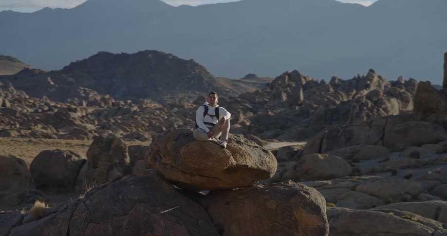 Man sitting on a large rock gazes at the mountainous landscape at sunset