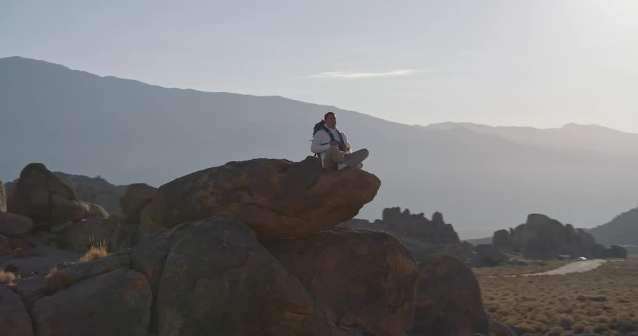 Man sitting crosslegged on rock in meditation pose facing mountains