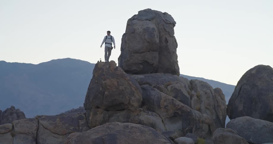Person standing on elevated rock surrounded by mountains under clear sky