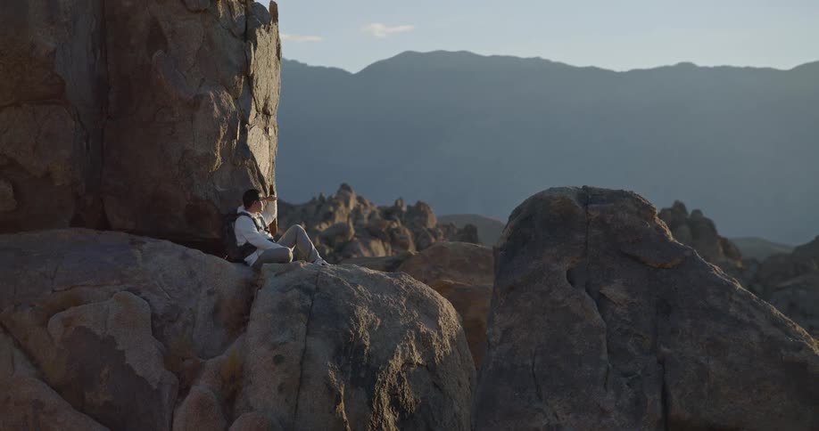 Person sitting on rock overlooking mountains at sunset