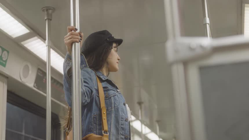 Woman with backpack standing inside subway car holding vertical pole under fluorescent lighting