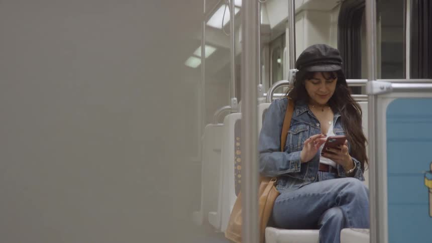 Woman sitting alone on public transport smiling while looking at her phone