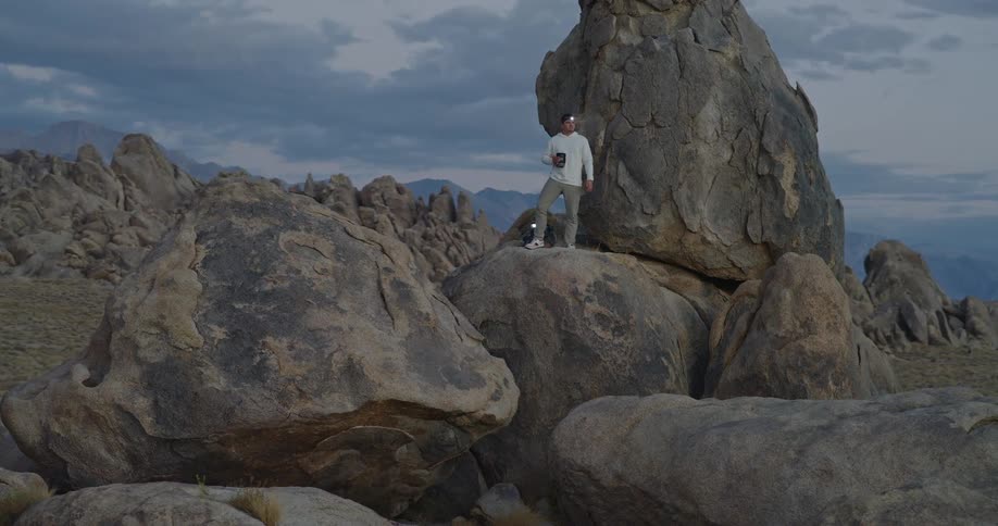 Man standing on rock using binoculars facing rocky mountains