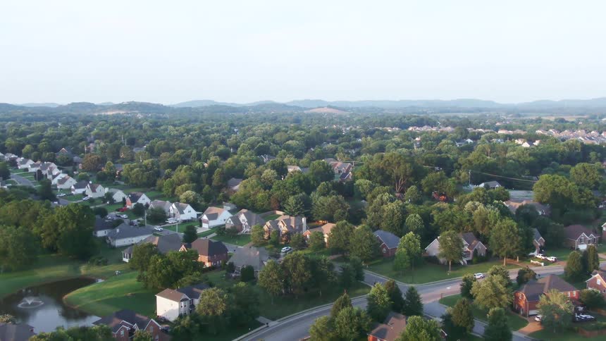 Aerial view of residential neighborhood surrounded by dense greenery with singlefamily homes and curving streets in a semirural setting