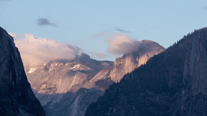 Granite cliff lit by sunset stands out among snowy mountains and clouds
