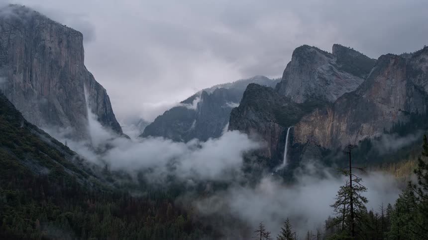 Waterfall cascades down rocky cliffs amid misty mountains and dense forest