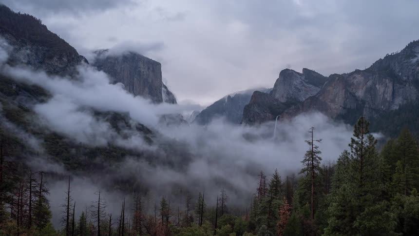 A mountain range covered in green vegetation under a foggy atmosphere on a cloudy day