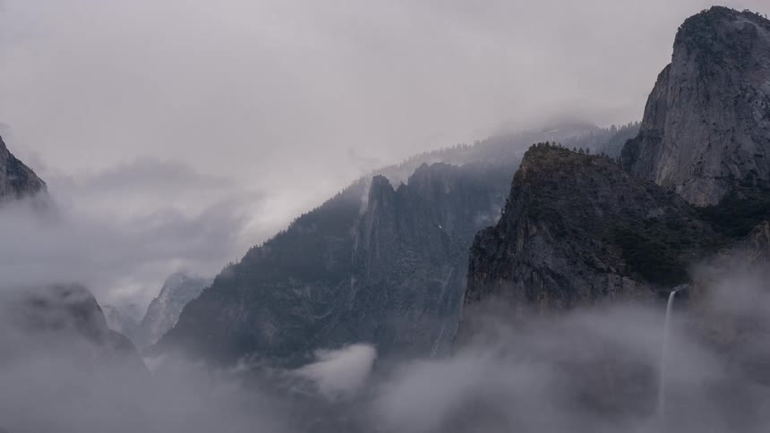 Waterfall cascades down rocky cliffs surrounded by misty mountains