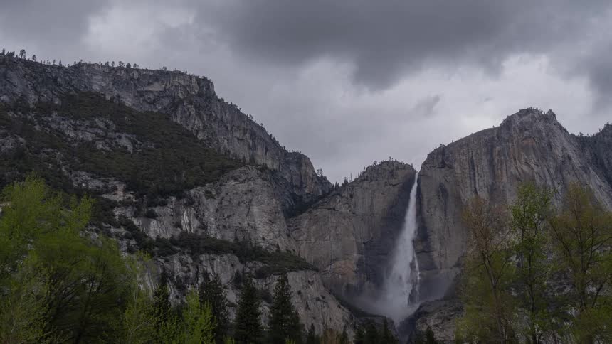 Waterfall plunges between granite cliffs with trees in the foreground
