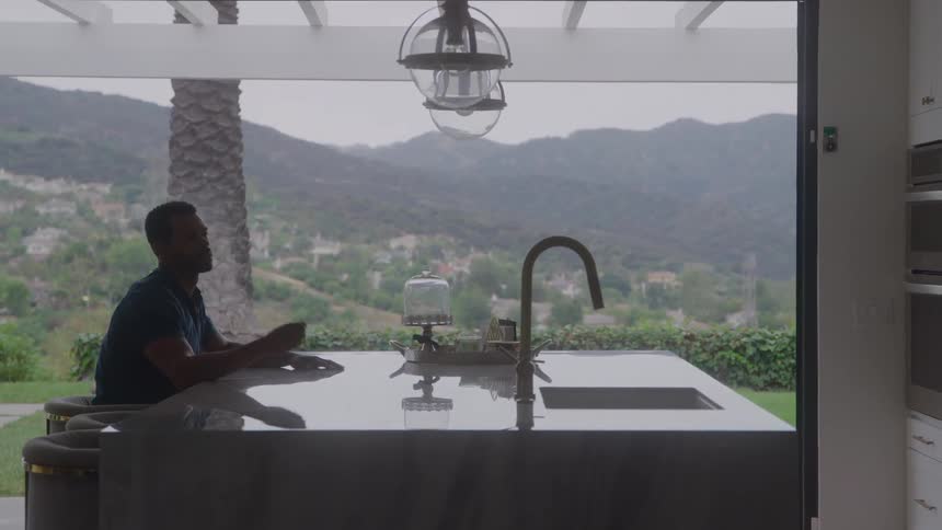 The video features a couple in a modern kitchen with a large marble island countertop they are silhouetted against a large window that offers a stunning view of rolling treecovered hills in the background