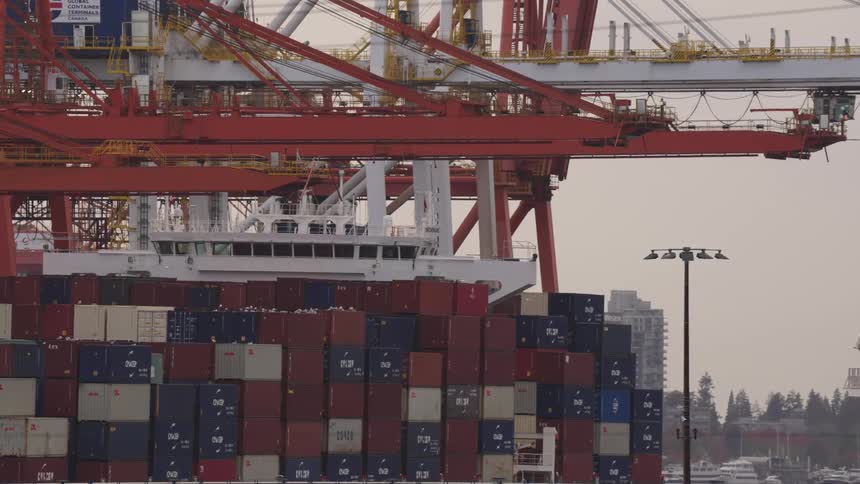 Stacked containers and cranes positioned at port with docked ship in the background