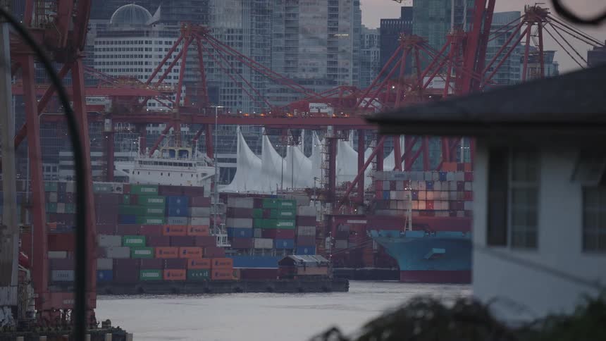 Colorful containers stacked at a port surrounded by cranes and buildings in the background