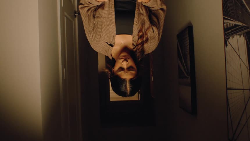 A woman stands in a dimly lit hallway her face reflecting a look of anxiety and apprehension as she holds a pregnancy test the camera slowly zooms and rotates intensifying the sense of nervous anticipation as she waits for the results