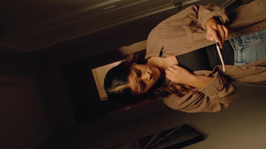 Anxious woman examining pregnancy test in softly lit hallway