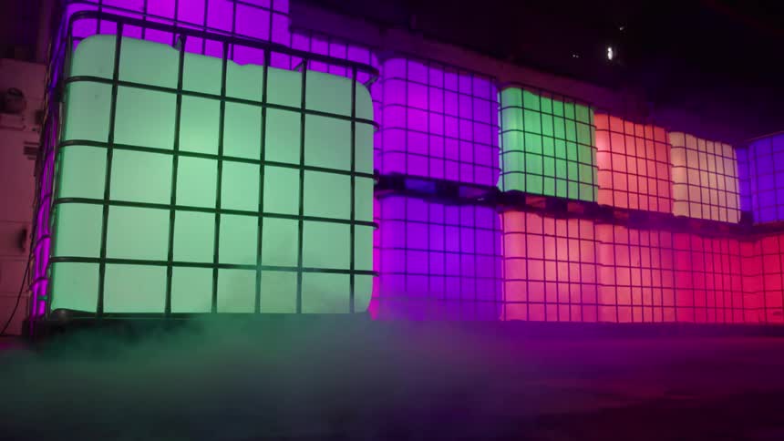 A fog machine runs nearby a backdrop made of colorfully illuminated cubes