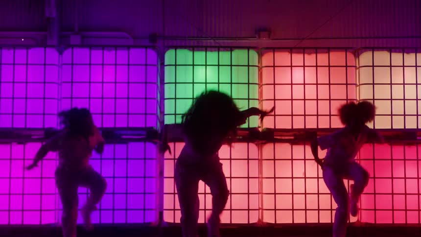 Three dancers perform a routine while backlit by colored panels illuminated from within