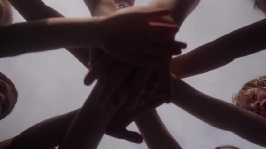 The children huddling put their hands together and raise them up