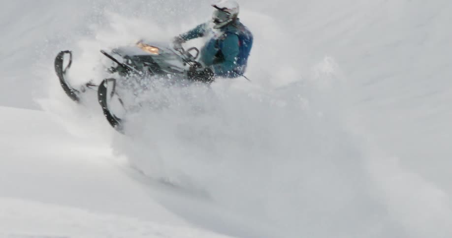 Person rides a snowmobile up a slope and into the air on a winter day