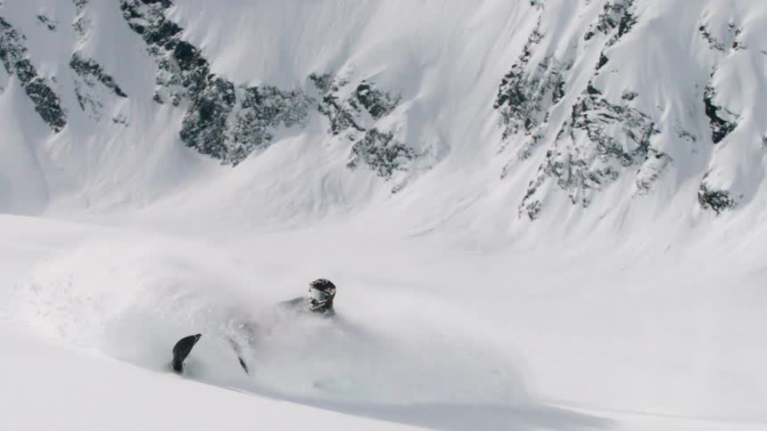 The man is turning back and forth cutting through the snow with the snowmobile