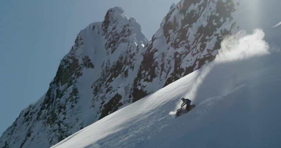 A person rides a snowmobile up and over a steep mountain on a sunny winter day