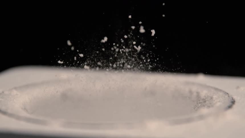 White particles spray into the air from a liquid filled container